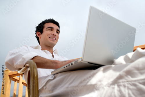 Photo: Man sat on garden chair with laptop Man sat on garden chair with laptop