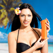 woman on the beach  holds orange sun tan lotion bottle.