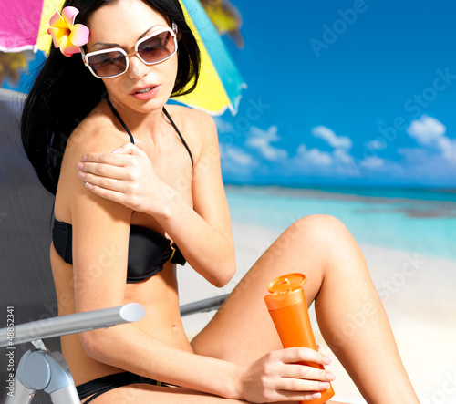 Photo: woman in bikini applying sun block cream on body woman in bikini applying sun block cream on body
