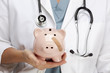 Foto: Doctor Holding Piggy Bank with Bandage on Face Doctor Holding Piggy Bank with Bandage on Face