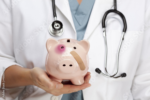 Photo: Doctor Holding Piggy Bank with Bruised Eye and Bandage Doctor Holding Piggy Bank with Bruised Eye and Bandage
