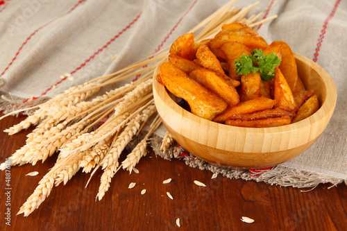 Photo: Appetizing village potatoes in bowl on wooden table close-up Appetizing village potatoes in bowl on wooden table close-up