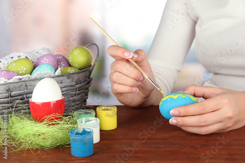 Photo: Young woman painting Easter eggs, on bright background Young woman painting Easter eggs, on bright background