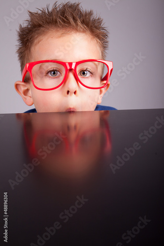 Photo: Five years old little cute boy hiding behind a table Five years old little cute boy hiding behind a table