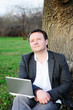 Businessman with laptop working under a tree