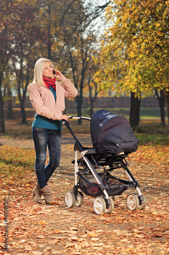 Photo: Young mother talking on a phone during a walk with her baby Young mother talking on a phone during a walk with her baby
