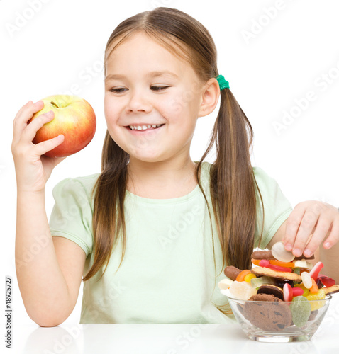 Photo: Little girl choosing between apples and sweets Little girl choosing between apples and sweets