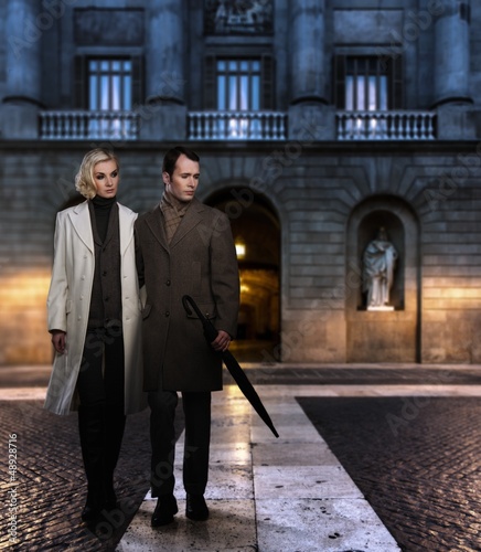 Photo: Elegant couple in coats against building facade in evening Elegant couple in coats against building facade in evening