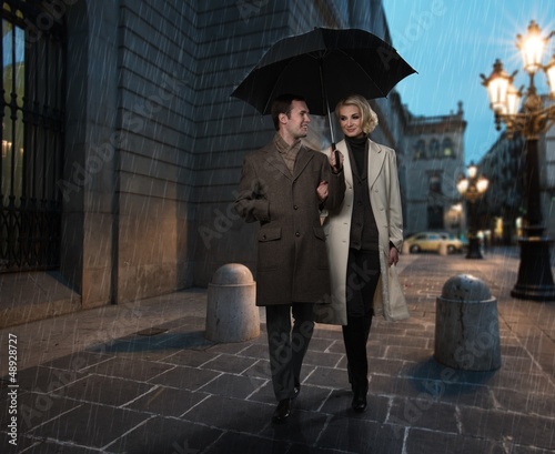Photo: Elegant couple with umbrella outdoors on rainy evening Elegant couple with umbrella outdoors on rainy evening