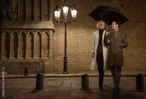 Photo: Elegant couple with umbrella outdoors on rainy evening Elegant couple with umbrella outdoors on rainy evening