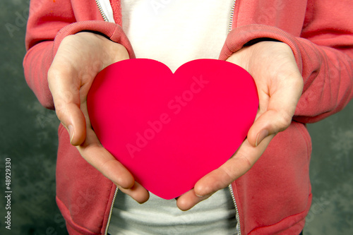 Photo: Closeup of teen girl in pink hoodie holding red heart Closeup of teen girl in pink hoodie holding red heart