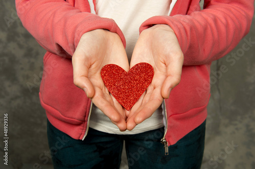 Photo: Closeup of teen girl in pink hoodie holding red heart Closeup of teen girl in pink hoodie holding red heart
