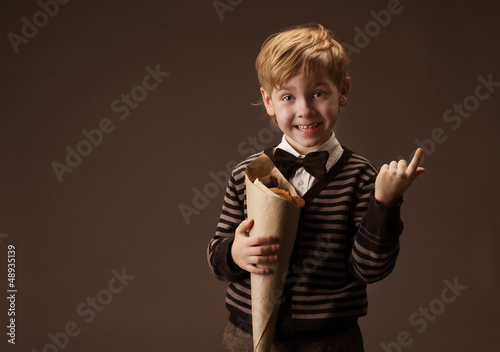 Photo: Child holding sweets in paper package. Boy in retro style. Brown Child holding sweets in paper package. Boy in retro style. Brown