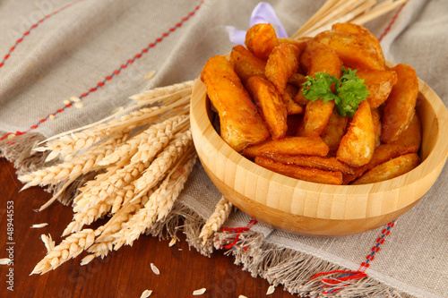 Photo: Appetizing village potatoes in bowl on wooden table close-up Appetizing village potatoes in bowl on wooden table close-up