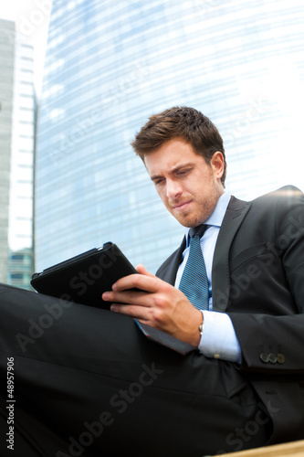 Photo: Businessman using a tablet on a bench in the city Businessman using a tablet on a bench in the city