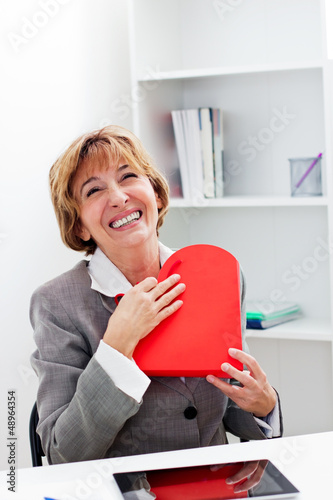 Photo: Businesswoman hugging a red heart present. Businesswoman hugging a red heart present.