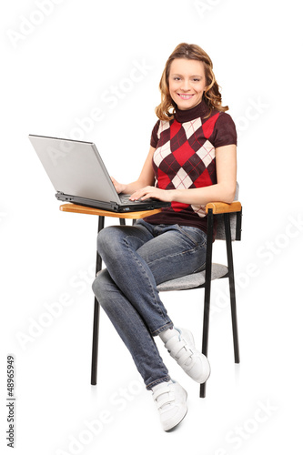 Photo: A smiling student female working on a laptop seated on a chair A smiling student female working on a laptop seated on a chair