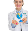 Photo: Closeup on smiling medical doctor woman holding pills and globe Closeup on smiling medical doctor woman holding pills and globe