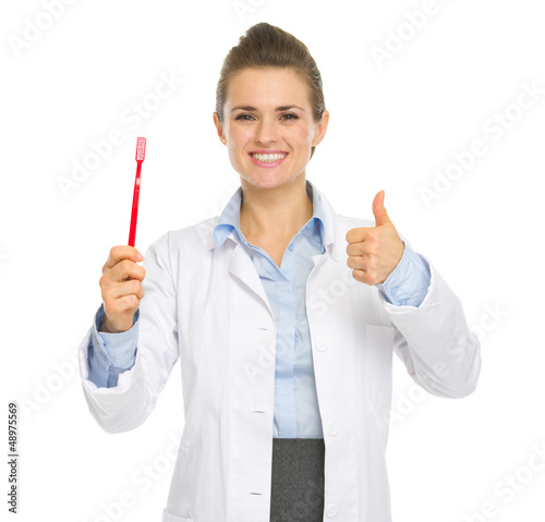Photo: Smiling medical doctor woman showing toothbrush and thumbs up Smiling medical doctor woman showing toothbrush and thumbs up