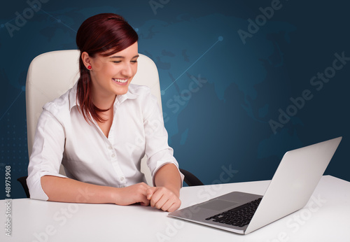 Photo: Young woman sitting at desk and typing on laptop Young woman sitting at desk and typing on laptop