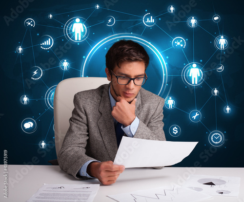 Photo: Businessman sitting at desk with social network icons Businessman sitting at desk with social network icons