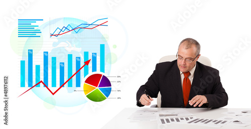 Photo: Businessman sitting at desk with statistics Businessman sitting at desk with statistics