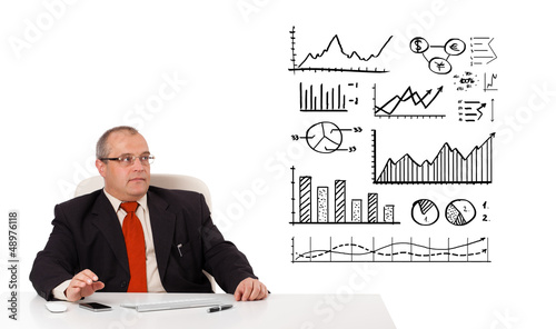 Photo: Businessman sitting at desk with diagrams and graphs Businessman sitting at desk with diagrams and graphs
