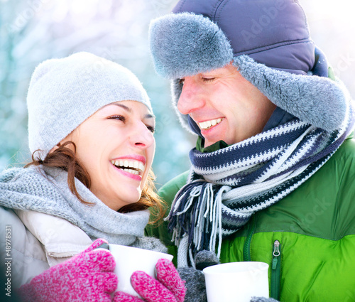Photo: Happy Couple with Hot Drinks Outdoors. Winter Vacation Happy Couple with Hot Drinks Outdoors. Winter Vacation