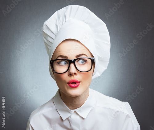 Photo: Close-up woman cook look round or hear something, over gray wall Close-up woman cook look round or hear something, over gray wall