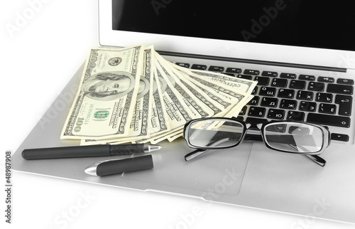 Photo: Money with glasses and pen on laptop isolated on white Money with glasses and pen on laptop isolated on white