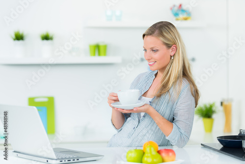 Photo: hübsche junge frau mit laptop in der küche hübsche junge frau mit laptop in der küche