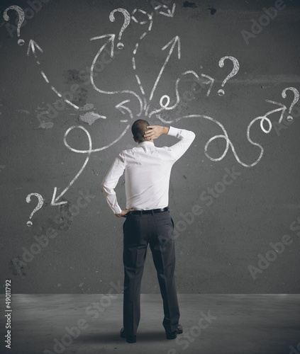 Photo: Businessman looking at arrows pointed in different directions Businessman looking at arrows pointed in different directions