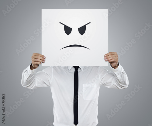 Photo: Young businessman holding card with a angry face on it Young businessman holding card with a angry face on it