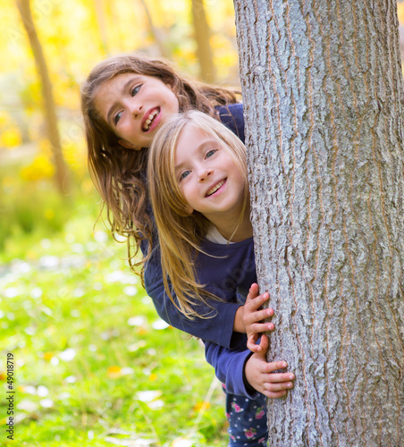 Photo: Autumn sister kid girls playing in forest trunk outdoor Autumn sister kid girls playing in forest trunk outdoor