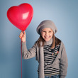 Young smiling girl with red heart balloon on blue background.