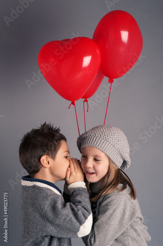 Photo: Young boy and girl with red heart balloons on grey background. Young boy and girl with red heart balloons on grey background.