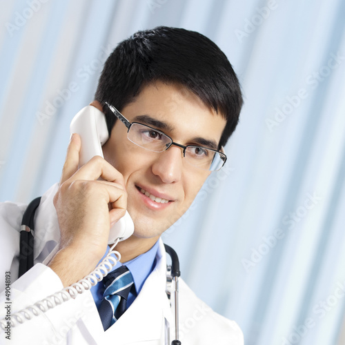 Photo: Young doctor on phone, at office Young doctor on phone, at office