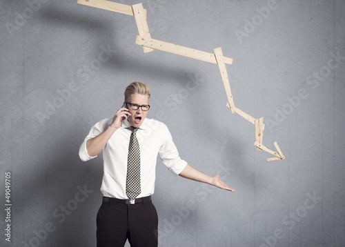 Photo: Angry businessman in front of graph pointing down. Angry businessman in front of graph pointing down.