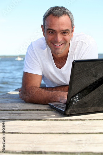 Photo: Man using his laptop on a wooden jetty Man using his laptop on a wooden jetty