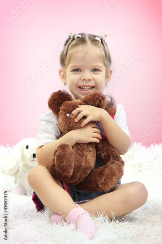 Photo: Cute little girl playing with toy bear, on pink background Cute little girl playing with toy bear, on pink background