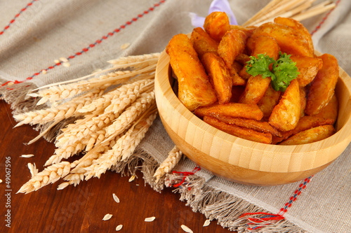 Photo: Appetizing village potatoes in bowl on wooden table close-up Appetizing village potatoes in bowl on wooden table close-up