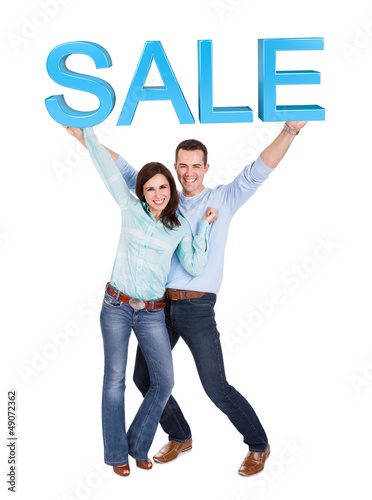 Photo: Happy young couple holding sale sign Happy young couple holding sale sign