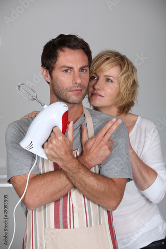 Photo: man wearing apron with hand mixer and wife man wearing apron with hand mixer and wife
