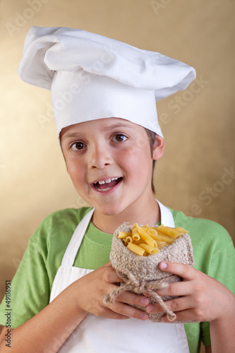 Photo: Happy boy with chef hat holding raw pasta in small sack Happy boy with chef hat holding raw pasta in small sack