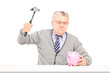 Angry mature man trying to break a piggy bank with a hammer