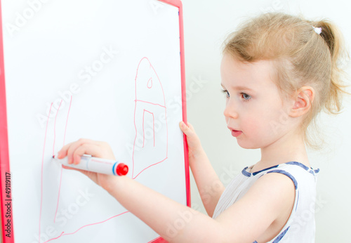 Photo: Pretty little girl drawing with red marker on a whiteboard Pretty little girl drawing with red marker on a whiteboard