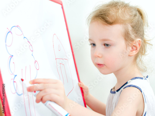 Photo: Pretty little girl drawing with red marker on a whiteboard Pretty little girl drawing with red marker on a whiteboard