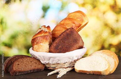 Photo: Fresh bread in basket on wooden table on natural background Fresh bread in basket on wooden table on natural background