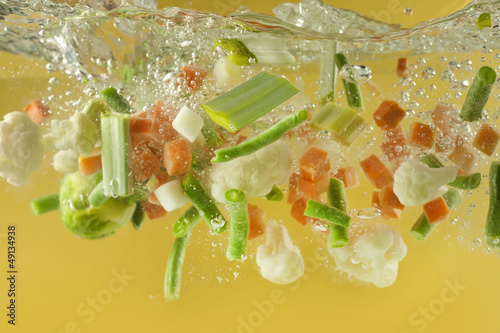 Photo: Vegetables splash in water soup cooking concept Vegetables splash in water soup cooking concept