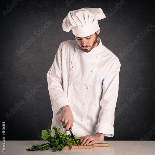Photo: Young cook man with uniform cutting vegetables Young cook man with uniform cutting vegetables